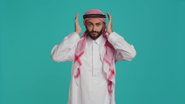 Adult does three wise monkeys sign on camera, wearing muslim traditional clothes and scarf. Young person covering his eyes, mouth and ears to illustrate metaphor symbol, concept.