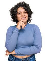 Fototapeta na wymiar Young hispanic woman with curly hair wearing casual clothes looking confident at the camera with smile with crossed arms and hand raised on chin. thinking positive.
