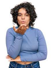 Young hispanic woman with curly hair wearing casual clothes looking at the camera blowing a kiss with hand on air being lovely and sexy. love expression.