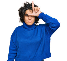 Young hispanic woman with curly hair wearing turtleneck sweater making fun of people with fingers...