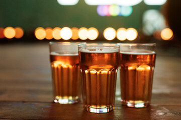 Three beer glasses on a wooden bar with colorful bokeh lights in the background