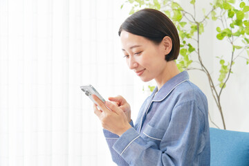 自宅でパジャマを着てスマホを使うミドルエイジの女性