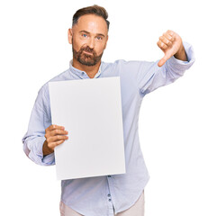 Handsome middle age man holding blank empty banner with angry face, negative sign showing dislike...