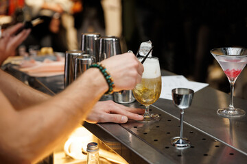 A skilled bartender pours ice into a glass with a shaken cocktail.