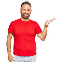 Handsome middle age man wearing casual red tshirt smiling cheerful presenting and pointing with palm of hand looking at the camera.