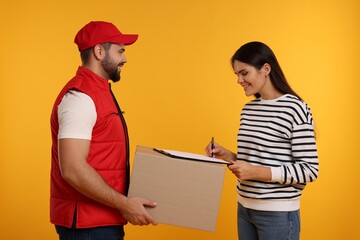 Happy young woman signing order receipt on orange background. Courier delivery