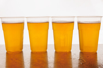 Plastic Disposable glasses of beer on a wooden surface and white background.