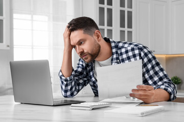 Man with laptop doing taxes at table in kitchen