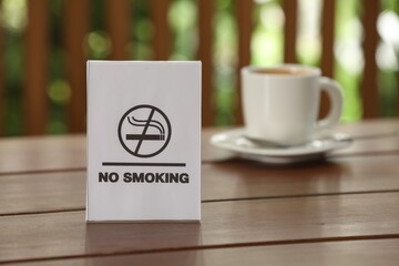 No Smoking sign and cup of drink on wooden table against blurred background, selective focus