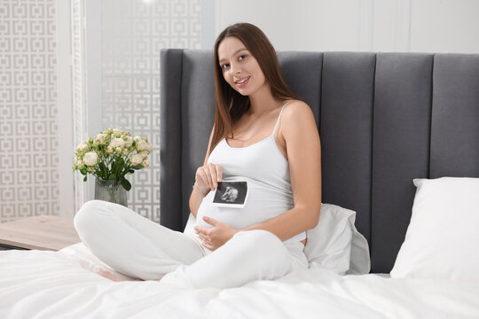 Pregnant woman with ultrasound picture of baby on bed indoors