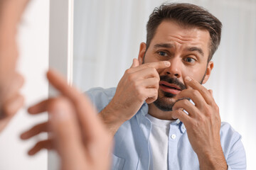 Confused man with skin problem looking at mirror indoors