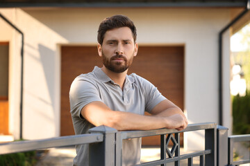Portrait of serious neighbour leaning on fence outdoors