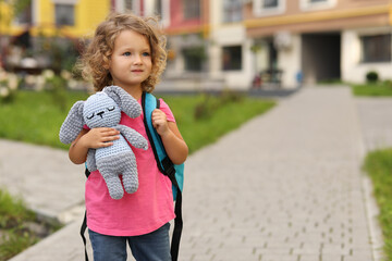 Little girl with toy walking to kindergarten outdoors. Space for text