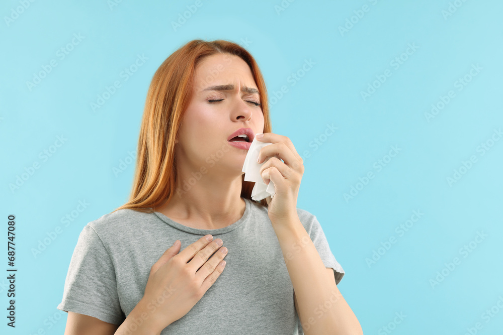 Poster Suffering from allergy. Young woman with tissue sneezing on light blue background, space for text