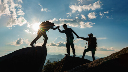 Silhouette of Asian teamwork  hikers climbing up mountain cliff and one of them giving helping hand...