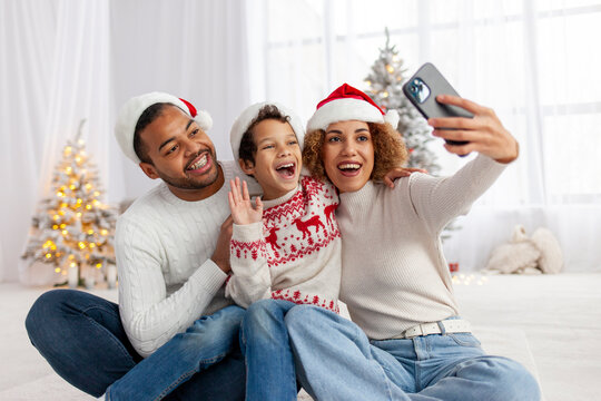 African-American family celebrates Christmas with their child and takes selfie on smartphone at home