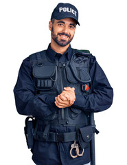 Young hispanic man wearing police uniform with hands together and crossed fingers smiling relaxed and cheerful. success and optimistic