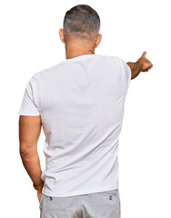 Middle age handsome man wearing casual white tshirt posing backwards pointing ahead with finger hand