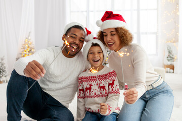 african american family in santa hats celebrate new year with child at home and set fire to sparklers and rejoice