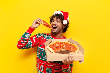young hungry hindu man in new year clothes eating pizza on yellow isolated background, hindu guy in...