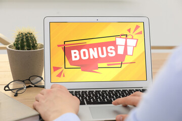 Bonus gaining. Man using laptop at table, closeup. Illustration of gift box and word on device...