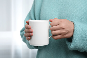Woman holding white mug indoors, closeup. Mockup for design