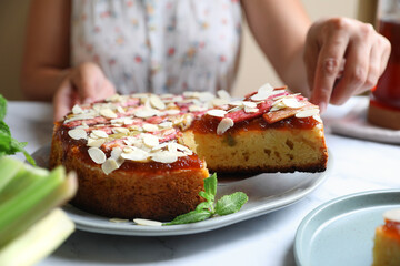 Woman taking piece of freshly baked rhubarb pie with almond flakes at white marble table, closeup