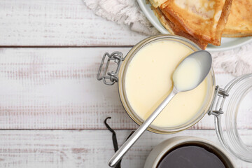 Tasty condensed milk, crepes and tea on white wooden table, flat lay. Space for text