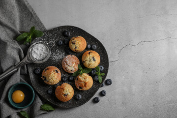 Delicious muffins with powdered sugar, blueberries and mint on light grey table, flat lay. Space for text