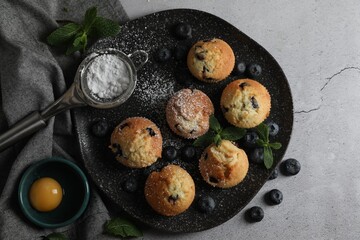 Delicious muffins with powdered sugar, blueberries and mint on light grey table, flat lay