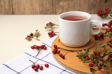 Cup with hawthorn tea and berries on beige table, space for text
