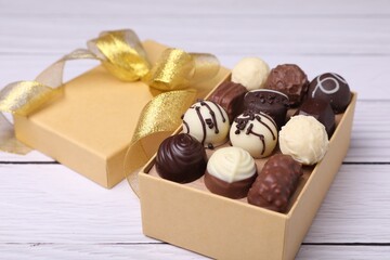 Box with tasty chocolate candies on white wooden table, closeup