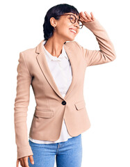 Young brunette woman with short hair wearing business jacket and glasses very happy and smiling looking far away with hand over head. searching concept.