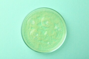 Petri dish with color liquid sample on light blue background, top view