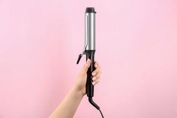 Hair styling appliance. Woman holding curling iron on pink background, closeup
