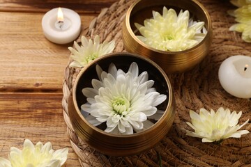 Fototapeta na wymiar Tibetan singing bowls, beautiful chrysanthemum flowers and burning candles on wooden table, closeup