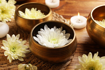 Fototapeta na wymiar Tibetan singing bowls, beautiful chrysanthemum flowers and burning candles on wooden table, closeup