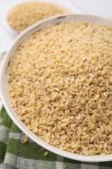 Raw bulgur in bowl on table, closeup