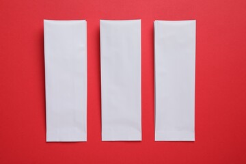 Three white paper bags on red background, flat lay. Space for text