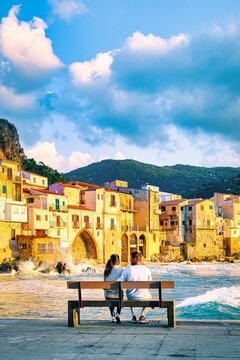 a couple of men and woman sitting on a bench at the waterfront on vacation in Sicily visiting the old town of Cefalu, sunset at the beach of Cefalu Sicily, the old town of Cefalu Sicilia Italy