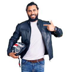 Young arab man holding motorcycle helmet pointing finger to one self smiling happy and proud