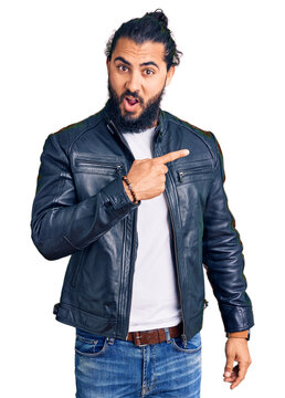 Young arab man wearing casual leather jacket surprised pointing with finger to the side, open mouth amazed expression.