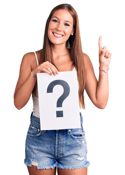 Young beautiful hispanic woman holding question mark surprised with an idea or question pointing finger with happy face, number one