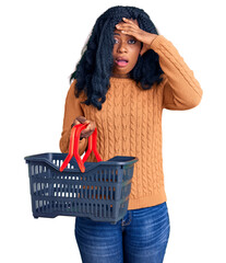 Beautiful african american woman holding supermarket shopping basket stressed and frustrated with hand on head, surprised and angry face