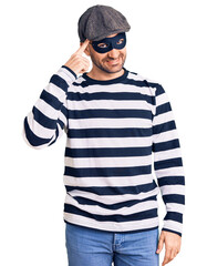 Young handsome man wearing burglar mask smiling pointing to head with one finger, great idea or thought, good memory