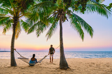 Najomtien Beach Pattaya Thailand, sunset at a tropical beach with palm trees. A couple of men and a woman mid age watching the sunset on the beach in a hammock with palm trees at Na Jomtien