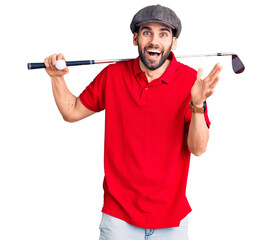 Young handsome man with beard playing golf holding club and ball celebrating victory with happy...