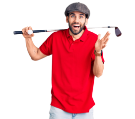 Young handsome man with beard playing golf holding club and ball celebrating victory with happy smile and winner expression with raised hands