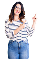 Beautiful young brunette woman wearing casual clothes and glasses smiling and looking at the camera pointing with two hands and fingers to the side.