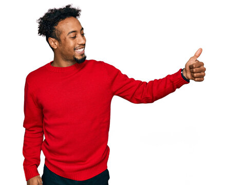 Young african american man with beard wearing casual winter sweater looking proud, smiling doing thumbs up gesture to the side
